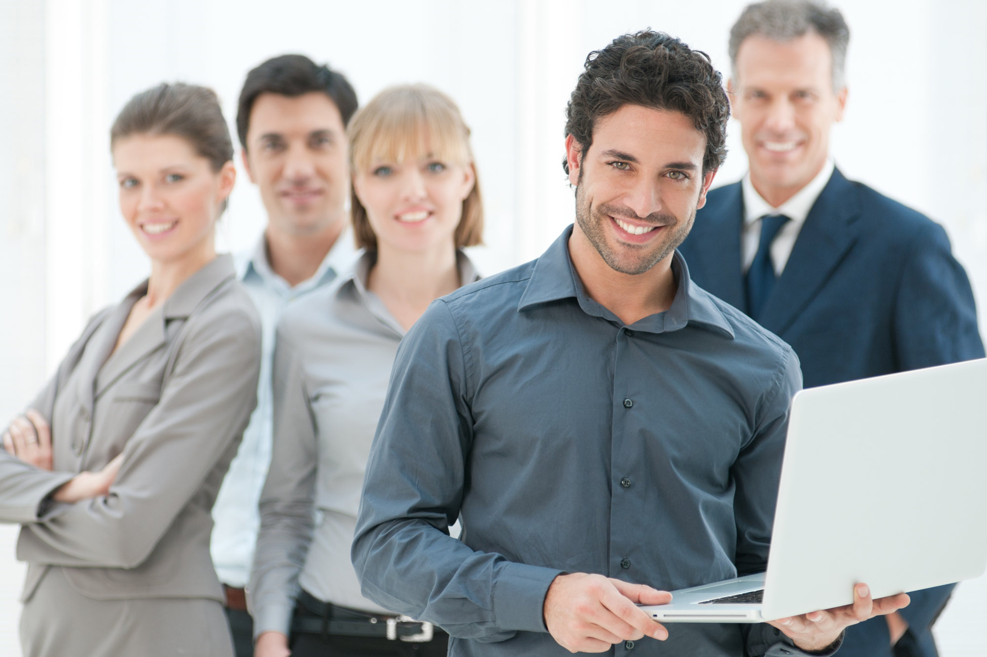 Happy businessman holding laptop, with his team in background