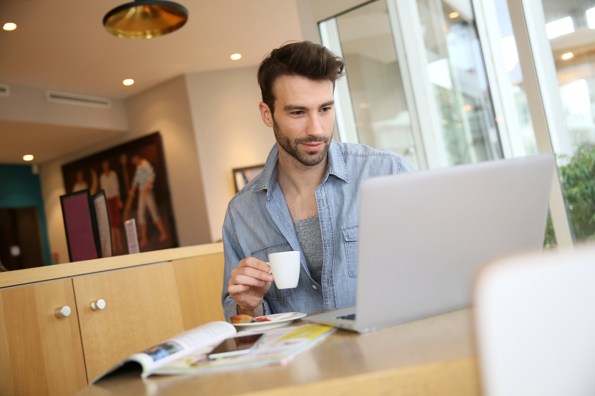 Man working on laptop computer from home while sipping coffee