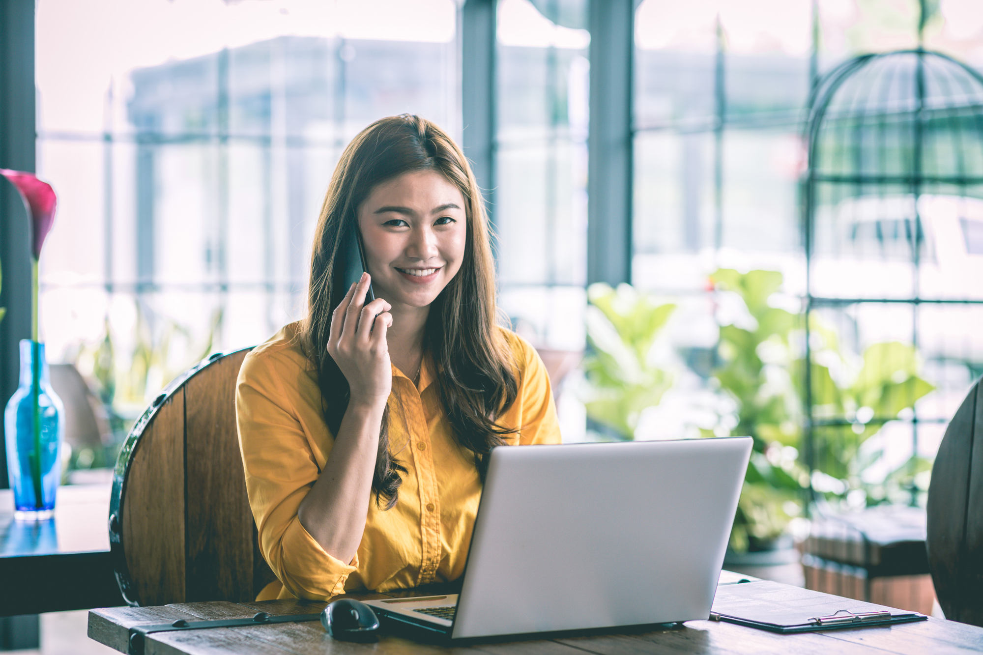 Smiling woman talking on smartphone while sitting in front of laptop