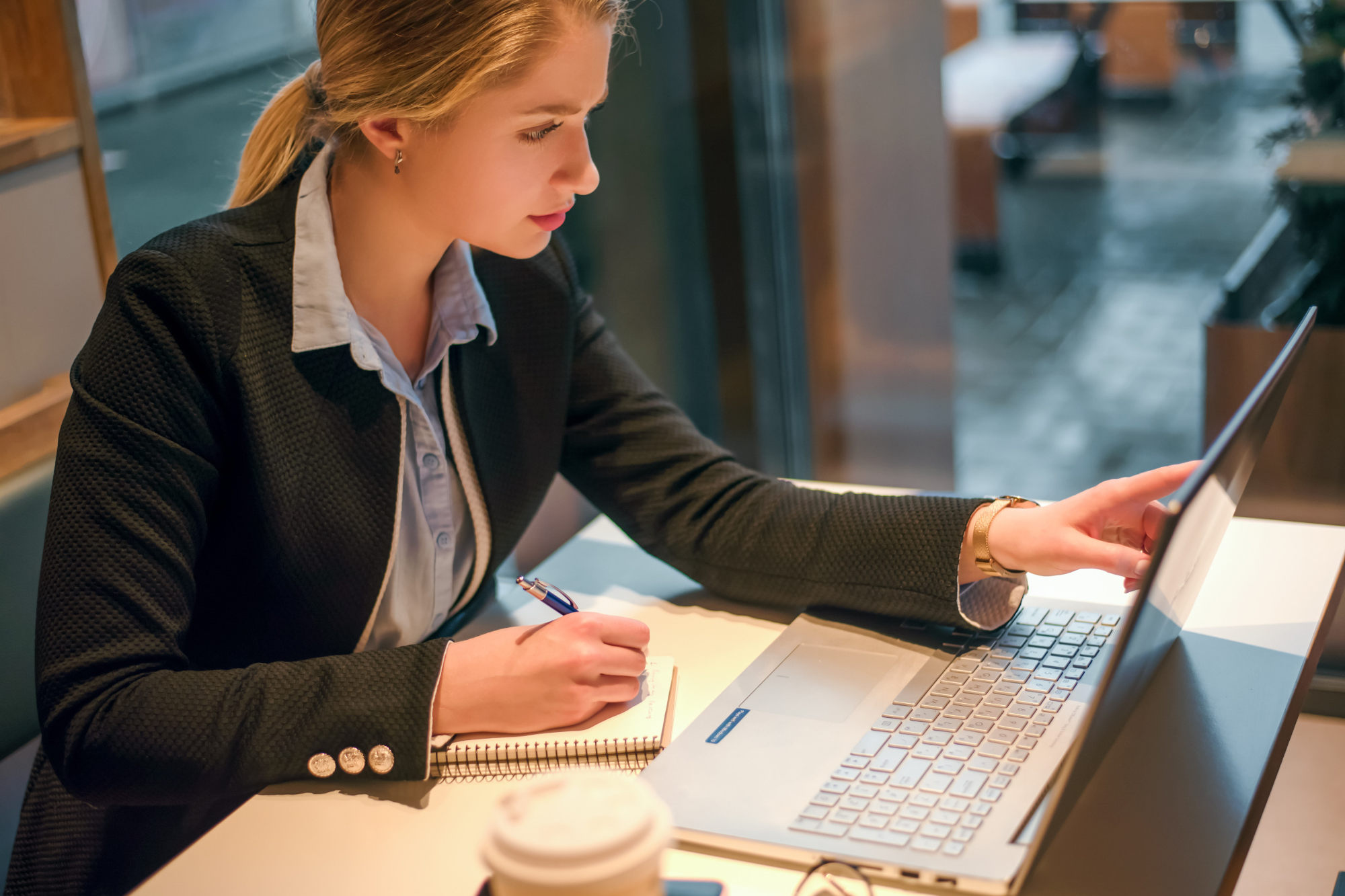 Woman using laptop while writing in notebook